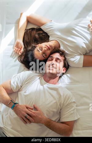 Ein glückliches junges Paar entspannt sich im Bett, lächelt und schaut sich an, während es einen zärtlichen Moment in gemütlicher Atmosphäre während eines ruhigen und faulen Wochenendes genießt Stockfoto