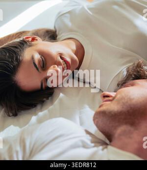 Zwei junge Liebende ruhen sich im Bett aus und genießen einen ruhigen Moment der Zärtlichkeit, fesselnder Romantik, emotionaler Verbindung und einer gemütlichen, familiären Atmosphäre Stockfoto