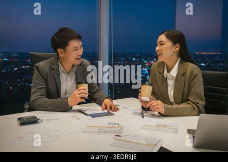 Zwei glückliche Geschäftskollegen treffen sich, führen ein zwangloses Gespräch und trinken abends Kaffee im modernen Büro Stockfoto