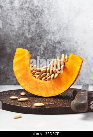 Frische Scheibe von „Mooregold“-Kürbis (Cucurbita maxima) mit Samen auf einem dunklen Holzbrett mit einem Messer. Stockfoto