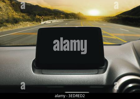 Car Dashboard blank Screen on Road Trip, Ein leerer Infotainment-Bildschirm auf einem Auto-Armaturenbrett mit Panoramablick auf die Autobahn bei Sonnenuntergang. Stockfoto