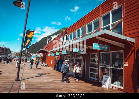 Juneau, Alaska - 25. Juli 2025: Touristen spazieren entlang der hölzernen Promenade vorbei an der Goldbelt Tram-Basisstation und dem Terminalgebäude mit einem großen cruis Stockfoto