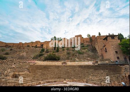 Weitwinkelblick auf das antike römische Theater mit Sitzgelegenheiten aus Stein vor den Festungsmauern von Alcazaba in Malaga, Spanien, unter bewölktem Himmel. Stockfoto