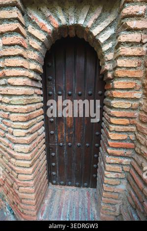 Nahaufnahme einer alten dunklen Holztür in einem schmalen Backsteinbogen. Verwitterte Ziegel und Metallnieten betonen das veraltete architektonische Detail. Stockfoto