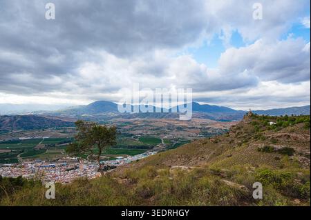 Breiter erhöhter Blick über ein ländliches Tal in der Nähe von Pizarra in Andalusien, Spanien, mit einer kleinen Stadt, umliegendem Ackerland, sanften Hügeln und fernen bergen Stockfoto