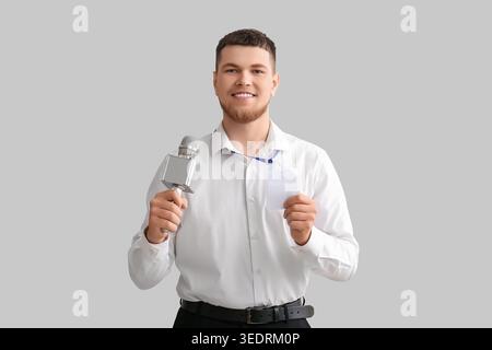 Männlicher Reporter mit Mikrofon und leerem Namensschild auf grauem Hintergrund Stockfoto
