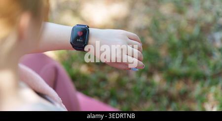 Asiatische Frau überprüft die Herzfrequenz auf Smartwatch während der Fitness im Freien Stockfoto