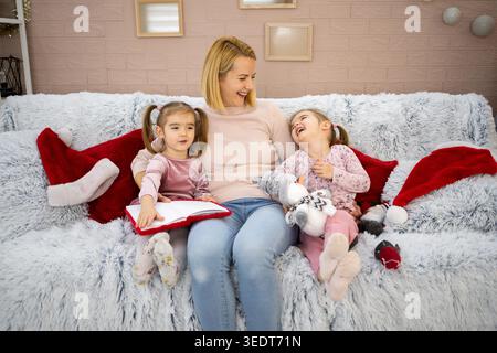 Mutter liest ihren Töchtern auf dem Sofa eine Weihnachtsgeschichte vor Stockfoto
