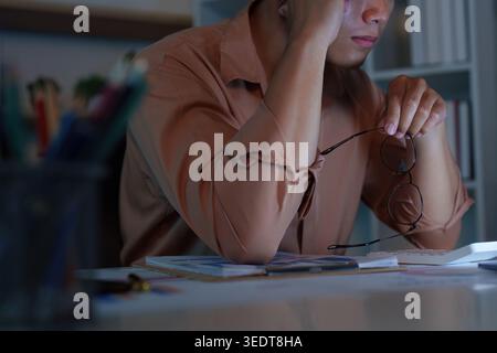 Asiatischer Mann mit Stress und Augenbelastung, der spät in der Nacht im Home Office arbeitet Stockfoto