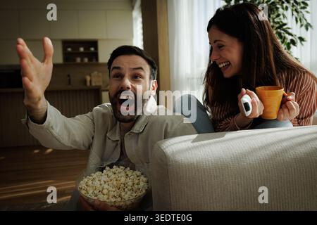 Ein Mann und eine Frau sitzen auf einer Couch, während sie ein Sportspiel anschauen und im Wohnzimmer jubeln Stockfoto