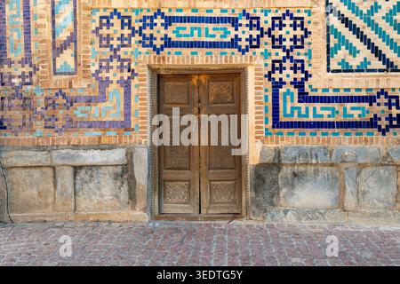Kunstvoll geschnitzte Holztür mit traditionellen usbekischen Majolika-Fliesen in blauen und türkisfarbenen Farben. Antike architektonische Details mit geometrischen Mustern Stockfoto