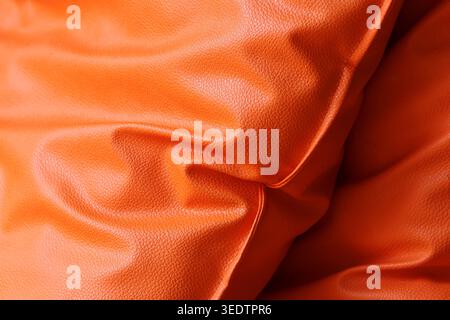Close Makroaufnahme aus leuchtend orangefarbenem, glänzendem Stoff mit glatten Falten und abstrakten Wellen für ein warmes, angenehmes Hintergrundmaterial für Elega Stockfoto