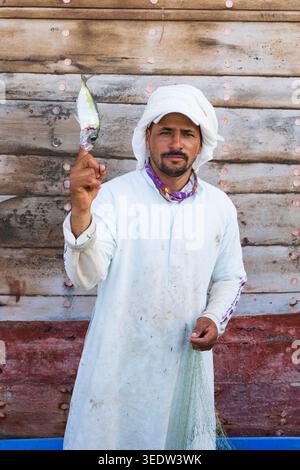 Ein ortsansässiger omanischer Fischer mit einem frischen Fisch am Finger am Dhow-Kai in Sur, Oman Stockfoto