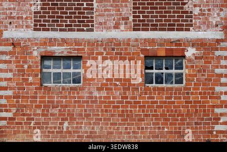 Freiliegende Ziegelfassade mit zwei beschädigten Fenstern eines verlassenen Industriegebäudes. Hintergrund und Textur. Stockfoto