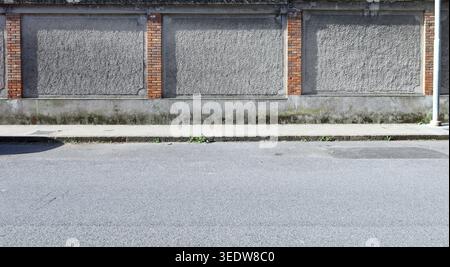 Raue Betonwand mit rauen Ziegelsäulen schleifen. Gefliester Bürgersteig und Straße vor dem Hotel. Städtischer Hintergrund für Kopierraum. Stockfoto