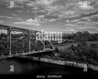 Schwarz-weiß aus der Vogelperspektive einer rostigen Metall-Fachwerkbrücke, die einen Kanal in der Nähe einer bewaldeten Landschaft in den Vororten von Chicago überquert Stockfoto