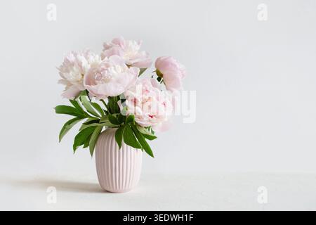Weicher rosafarbener Pfingstrosenstrauß in pastellfarbener Keramikvase auf weißem Hintergrund mit Kopierraum Stockfoto