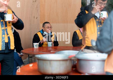 Taipeh, Taiwan - 29. März 2025: Tempelfreiwillige in gelben Westen essen bei einem gemeinsamen Bankett im Freien aus Pappbechern an roten Klapptischen. Stockfoto
