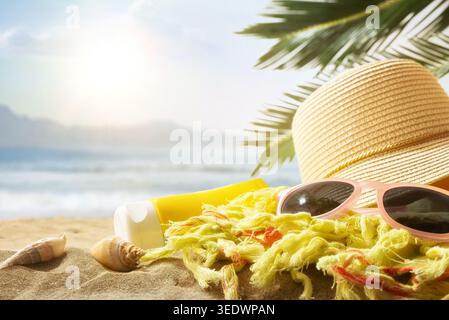 Strohhut, Sonnenbrille, Sonnencreme und Schal am Sandstrand mit Meereswellen und Palmblättern unter hellem Sommersonnenlicht. Stockfoto