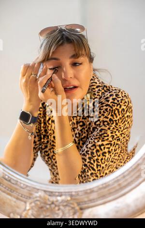 Attraktive Frau, die Make-up mit Leopardenmuster am Spiegel in Elgin, Westkap, Südafrika aufträgt Stockfoto