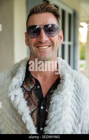 Mann in Sonnenbrille und Kunstpelzmantel lächelt auf der Mottoparty zum 50. Geburtstag in Elgin, Westkap, Südafrika Stockfoto