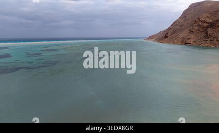 Weite Küstenlandschaft mit türkisfarbenem Flachwasser, Korallenriff, felsiger Wüstenküste und bewölktem Himmel; ruhige abgelegene Bucht ideal für Stockfoto