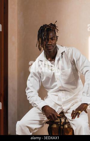 Junger schwarzer Mann mit weißem Hemd und Hose, der mit Dreadlocks und Perlen posiert Stockfoto