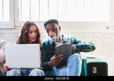 Vielfältige junge Menschen, die sich ein Tablet und ein Notebook ansehen, zusammenarbeiten und interagieren Stockfoto