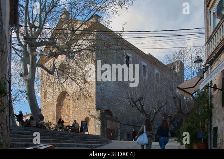 Valldemossa, Spanien - 6. Mai 2026: Touristen spazieren durch die Steinstraßen von Valldemossa, vorbei am historischen Charterhouse-Gebäude und einem Café im Freien Stockfoto
