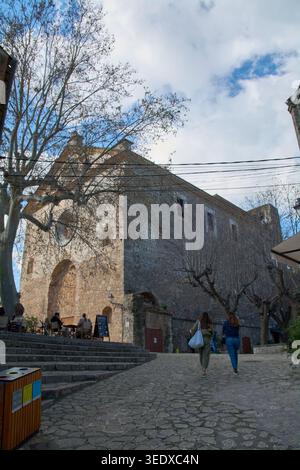 Valldemossa, Spanien - 6. Mai 2026: Zwei Frauen gehen auf einem Kopfsteinpflasterweg in Richtung des historischen Charterhauses von Valldemossa unter einem bewölkten Himmel in den s Stockfoto