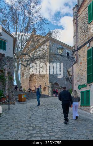 Valldemossa, Spanien - 6. Mai 2026: Touristen gehen entlang einer Kopfsteinpflasterstraße in Richtung des historischen Charterhauses von Valldemossa, wo Menschen fotografieren Stockfoto
