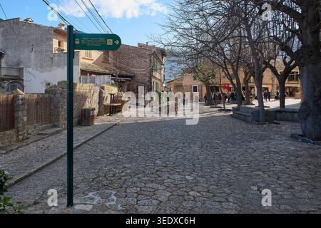 Valldemossa, Spanien - 6. Mai 2026: Ein weites Bild von einem sonnendurchfluteten Kopfsteinpflasterplatz in Valldemossa zeigt ein grünes Schild, das auf das echte Cartuja museum zeigt Stockfoto