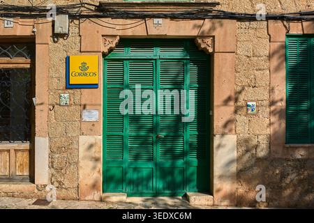 Valldemossa, Spanien - 6. Mai 2026: Eintritt zum lokalen Postamt mit einem leuchtend gelben Correos-Logo neben traditionellen grünen Lamellen Stockfoto