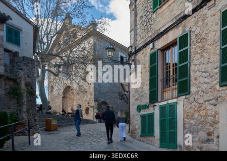 Valldemossa, Spanien - 6. Mai 2026: Touristen gehen entlang einer Kopfsteinpflasterstraße in Richtung des historischen Charterhauses von Valldemossa mit traditionellem Stein Stockfoto