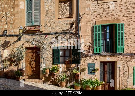 Valldemossa, Spanien - 6. Mai 2026: Sonnenverwöhnte Steinhäuser entlang einer engen Gasse auf Mallorca mit berühmten grünen Fensterläden, Kletterweinen und Stockfoto