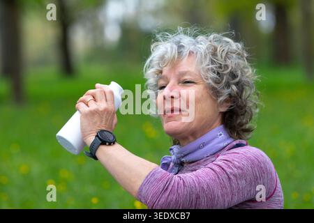 Die Seniorin trinkt nach dem Training im Freien Flüssigkeit aus einer Wasserflasche Stockfoto