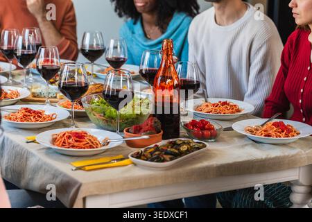 Eine Gruppe von Personen, die sich eine Pasta-Mahlzeit mit Wein an einem Tisch teilen, um ihre Freundschaft zu feiern Stockfoto