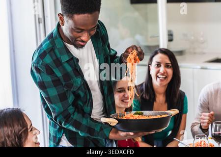 Verschiedene Freunde, die zu Hause eine Pasta-Mahlzeit genießen, Essen und Gesellschaft genießen Stockfoto