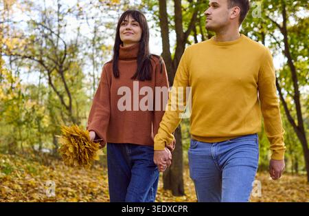 Lächelnde Liebhaber, die Hände auf einem grünen Pfad halten, genießen Romantik im Herbstpark Stockfoto