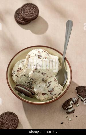 Cremiges Stracciatella-Eis, serviert in einer Schüssel mit Schokoladenkeksen auf einem sonnigen Tisch, Blick von oben. Italienisches Eisdessert mit Schokoladenstückchen Stockfoto