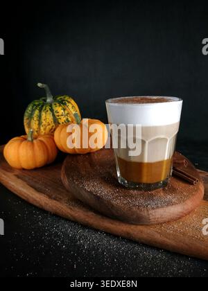 Warmer, cremiger Latte in den Händen gehalten mit eleganter Herzlattekunst auf dunklem, strukturiertem Hintergrund. Stockfoto