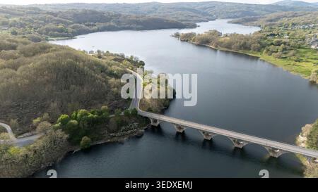 Aus der Vogelperspektive zeigt den Stausee prada, eine Bogenbrücke und eine gewundene Straße in einem veiga, ourense, galicien, spanien Stockfoto