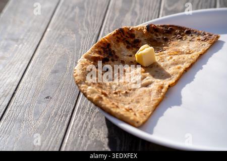 Traditionelle indische Aloo Paratha serviert mit schmelzender Butter auf einem Teller bei einer Dhaba am Straßenrand während der sonnigen Frühstückszeit. Stockfoto