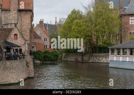 Brügge, Belgien - 3. April 2026: Blick auf den Kanal von Rozenhoedkaai mit historischen Backsteinhäusern, grünen Bäumen und Architektur am Wasser. Mittelalterlich Stockfoto