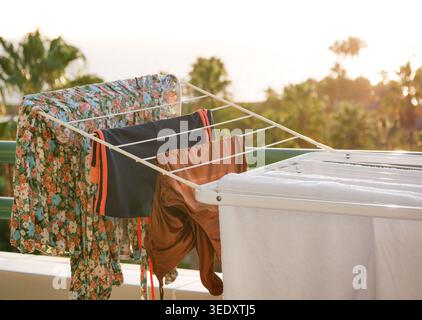 Wäscherei und Strandkleidung trocknen auf einem Balkonständer bei Sonnenuntergang. Gemütliche Reise-Lifestyle-Szene mit tropischem Hintergrund, Sonnenlicht, Urlaubsstimmung und Öko-Frien Stockfoto