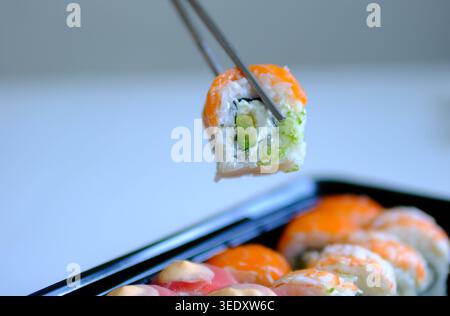 Sushi-Rolle in Sojasauce auf schwarzem Hintergrund, vertikales Nahaufnahme-Video. Der Mann isst Sushi-Brötchen mit Stäbchen, während er es in Soße einweicht. Philadelphia Sushi mit Lachs Stockfoto