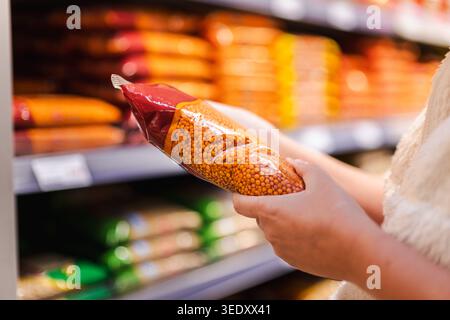 Frau, die verpackte rote Linsen im Supermarktgang wählt, Kunde hält trockene Leguminosen beim Einkaufen für gesunde Lebensmittelzutaten Stockfoto