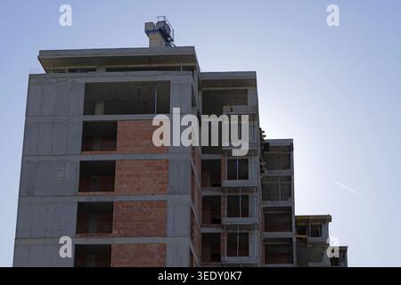 Mehrstöckiges Wohngebäude im Bau mit Sichtbetonkonstruktion, roten Ziegelwänden und Stufenterrasse, die unter warmen Temperaturen erfasst wird Stockfoto