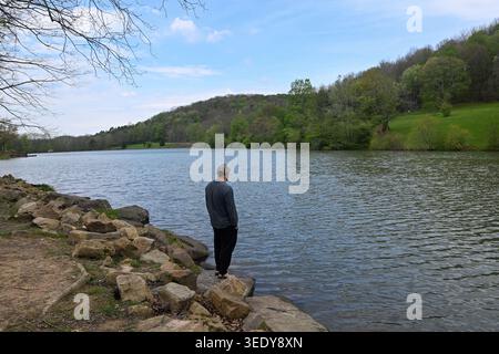 Mann, der auf dem Ufer des Sees steht, mit Blick auf grüne Hügel und grünes Gras mit großen Felsen und Schlammquellen in pennsylvania Stockfoto