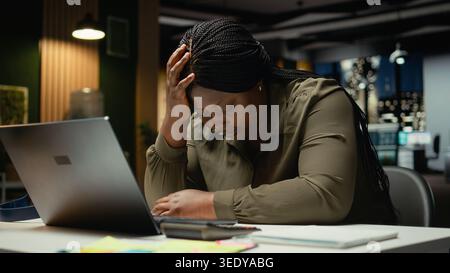 afroamerikanerin, die nach Stunden am Schreibtisch müde wurde und mit dem Kopf in der Hand einschlief. Überforderte ängstliche und ermüdete Arbeiter sind mit Burnout und geistiger Dunst konfrontiert. Kamera A.. Stockfoto